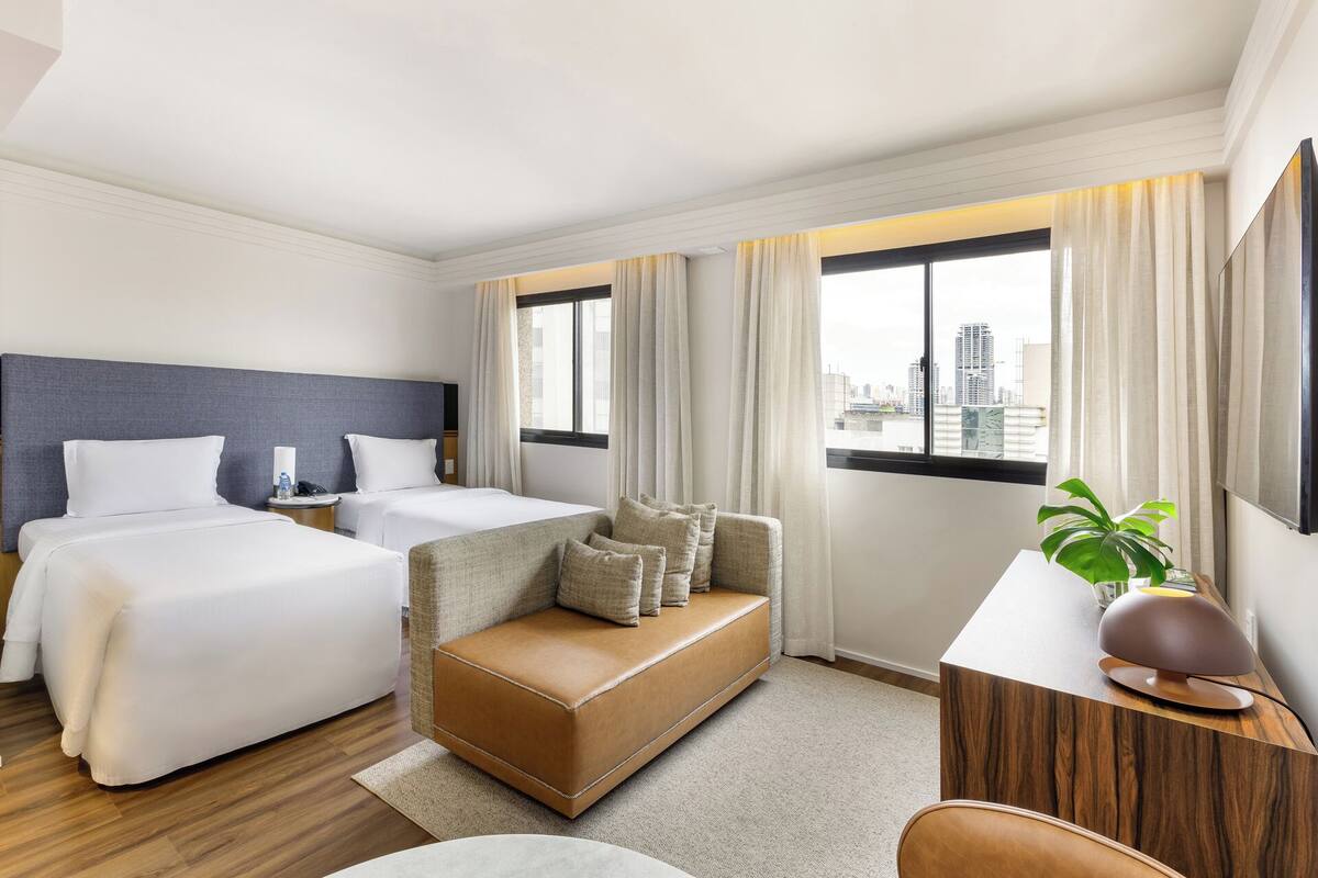 Habitación de hotel con dos camas, un sofá, un escritorio y vistas a la ciudad.