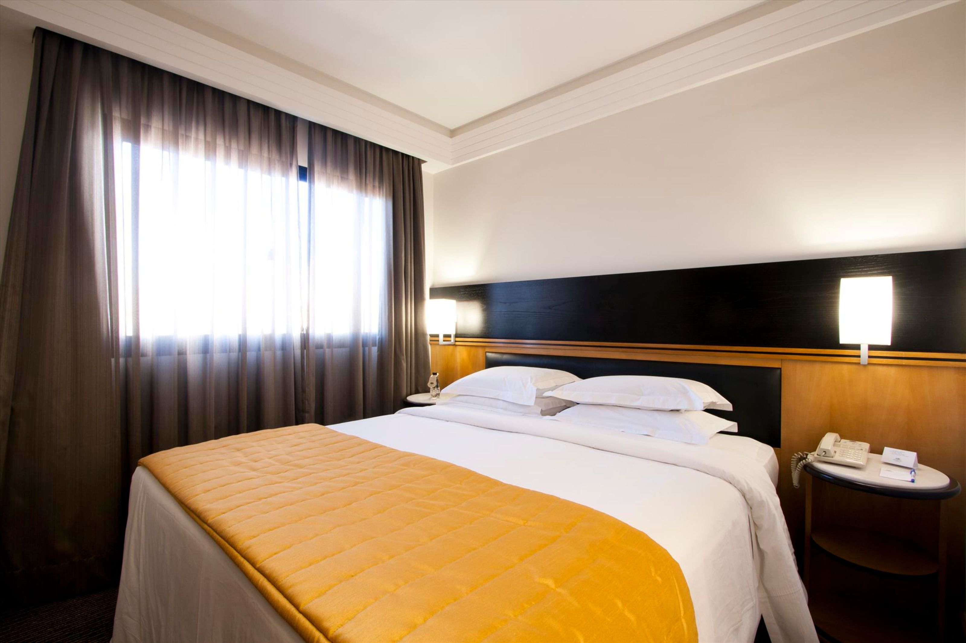 A hotel room with a large bed, a bedside table with a phone, and a window with curtains.