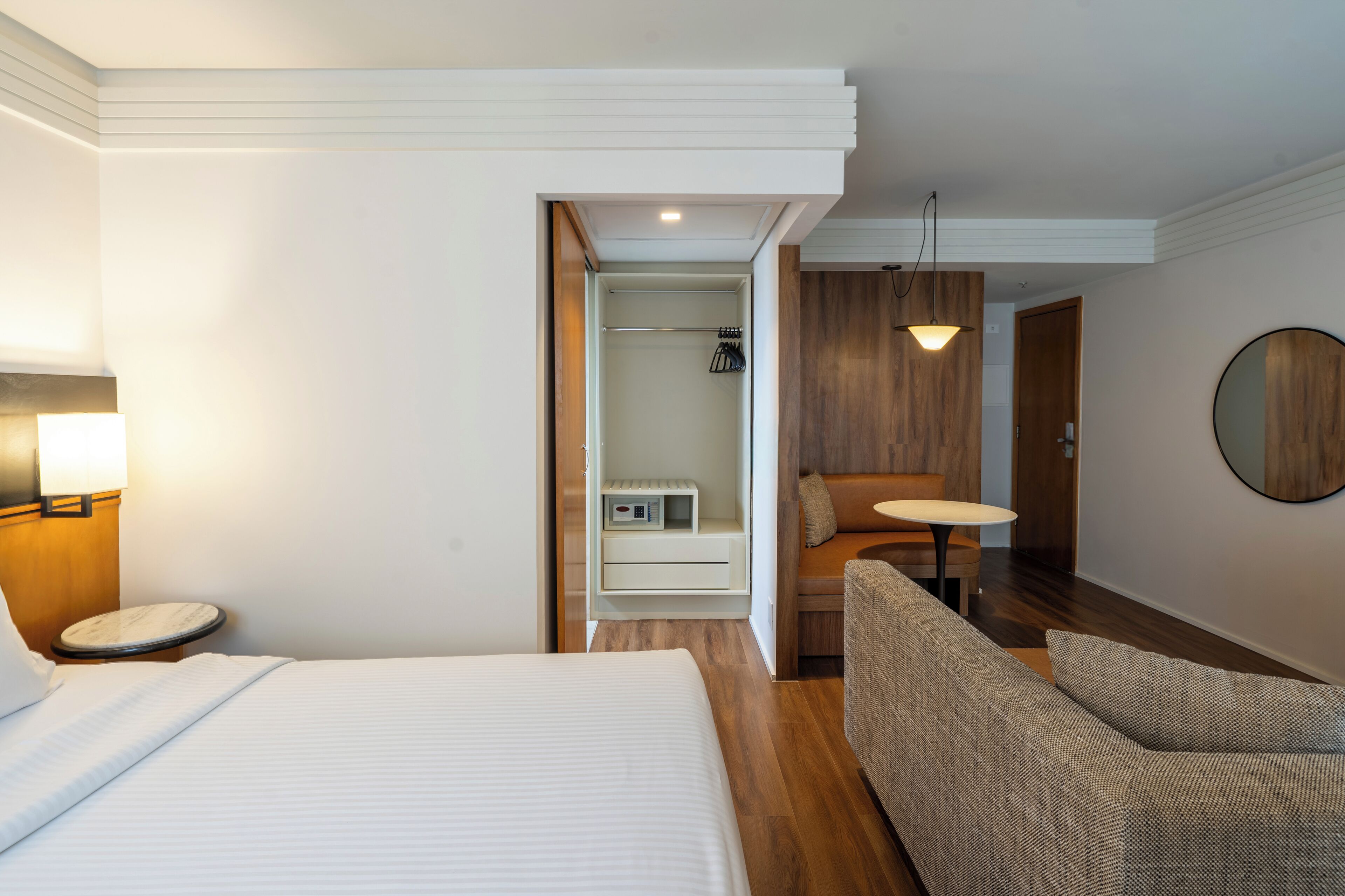 A hotel room with a bed, a sofa, a small table, a mirror, and a walk-in closet.