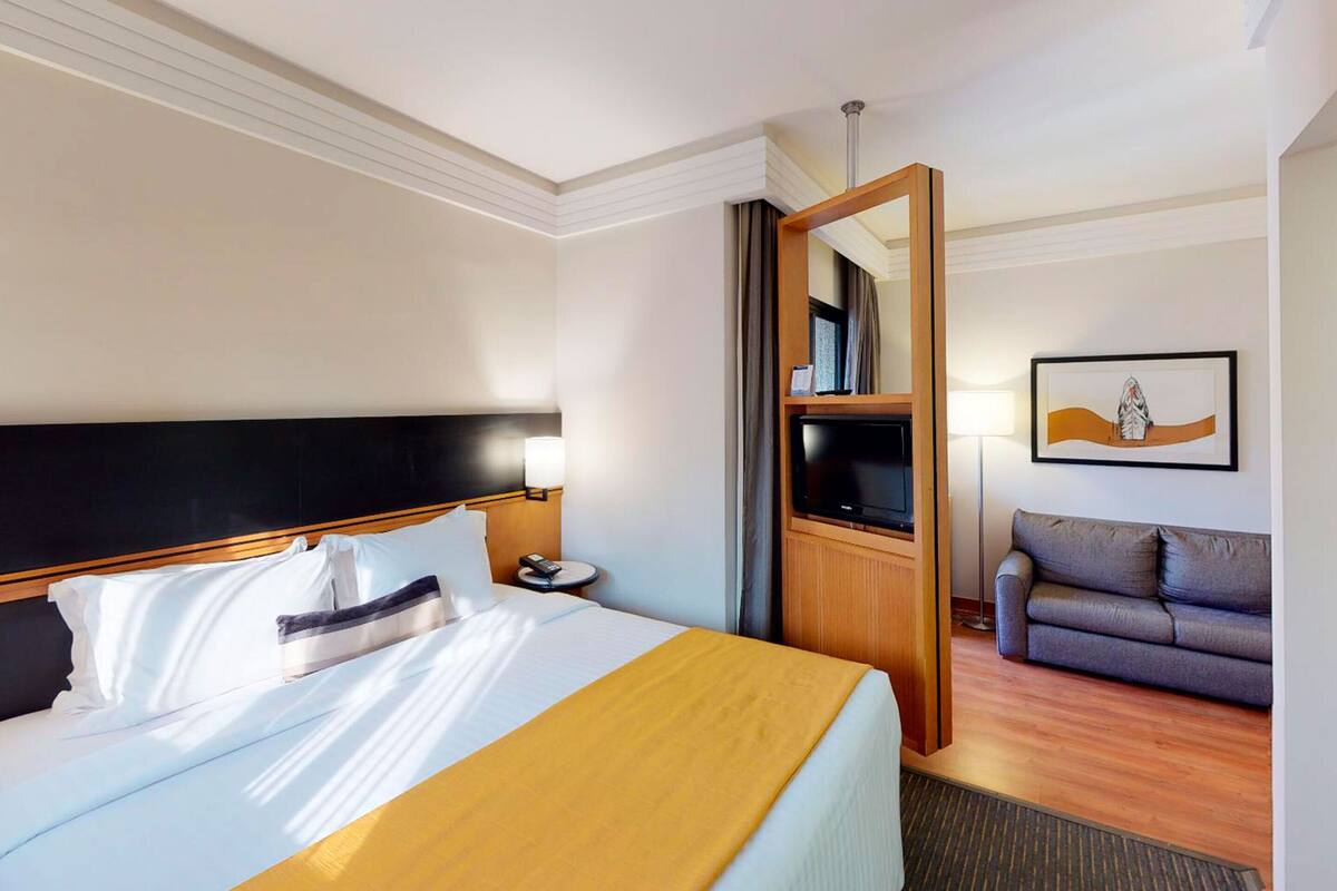 Una habitación de hotel con una cama, televisión, sofá y un cuadro en la pared.