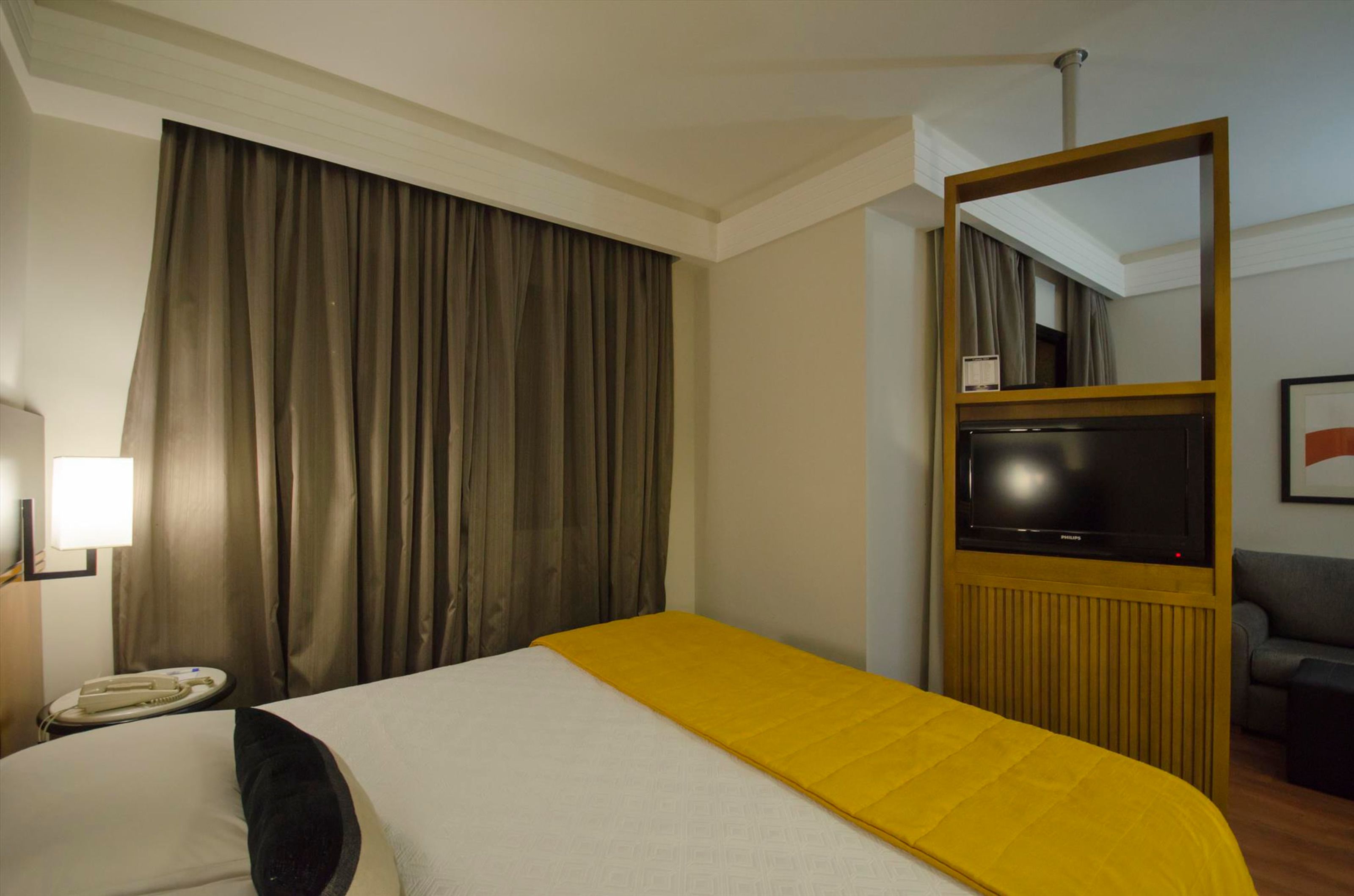 Una habitación de hotel con cama, televisor, espejo, sofá y teléfono.