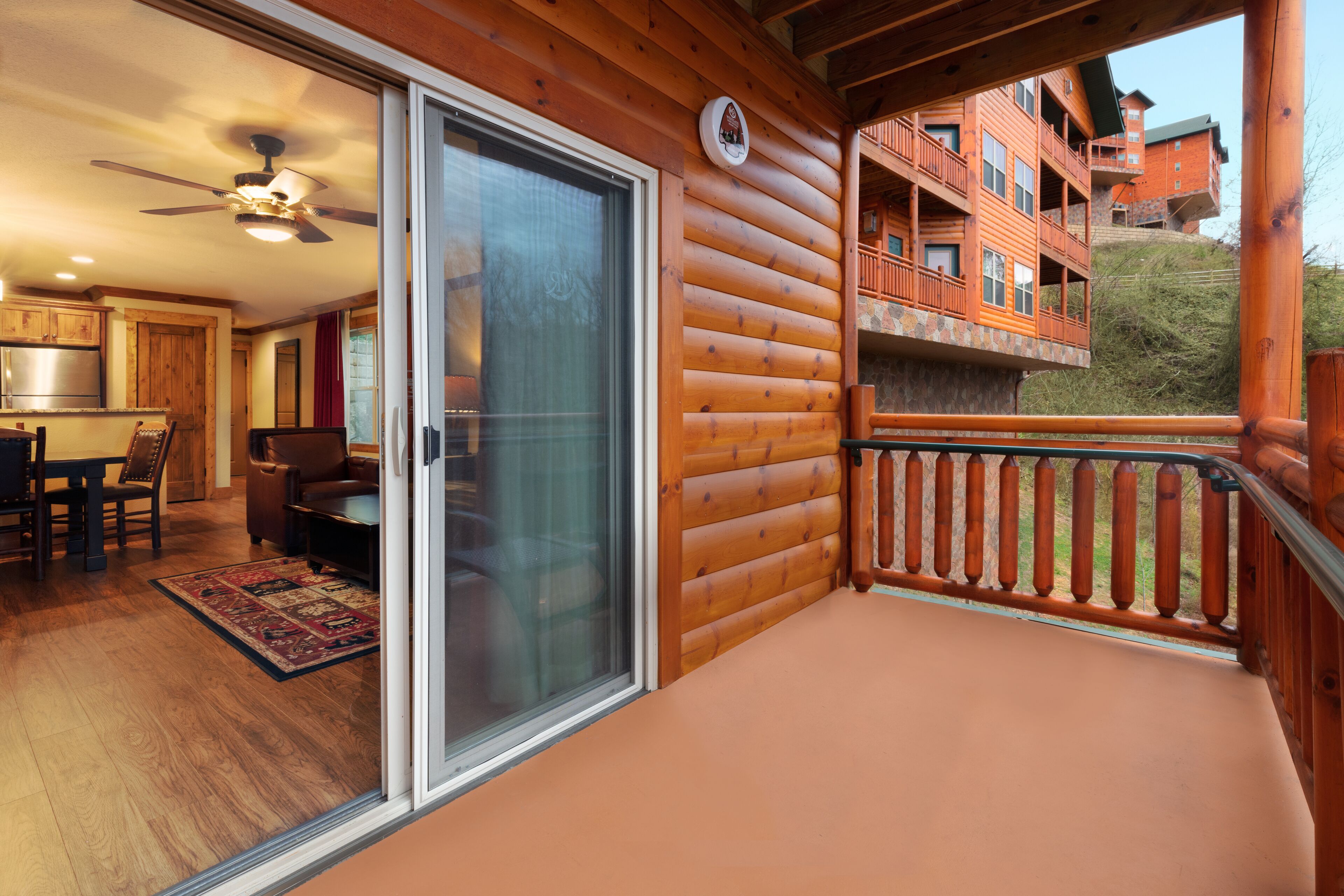 Une cabane en bois dotée d’un balcon, d’une porte-fenêtre coulissante, d’un ventilateur de plafond et d’un coin cuisine avec des placards en bois.