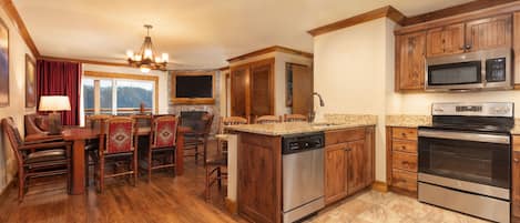 A kitchen with wooden cabinets, a built-in microwave, a dishwasher, and a dining area with chairs and a table.