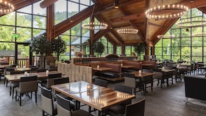 A spacious restaurant with high ceilings, large windows, and wooden tables and chairs.