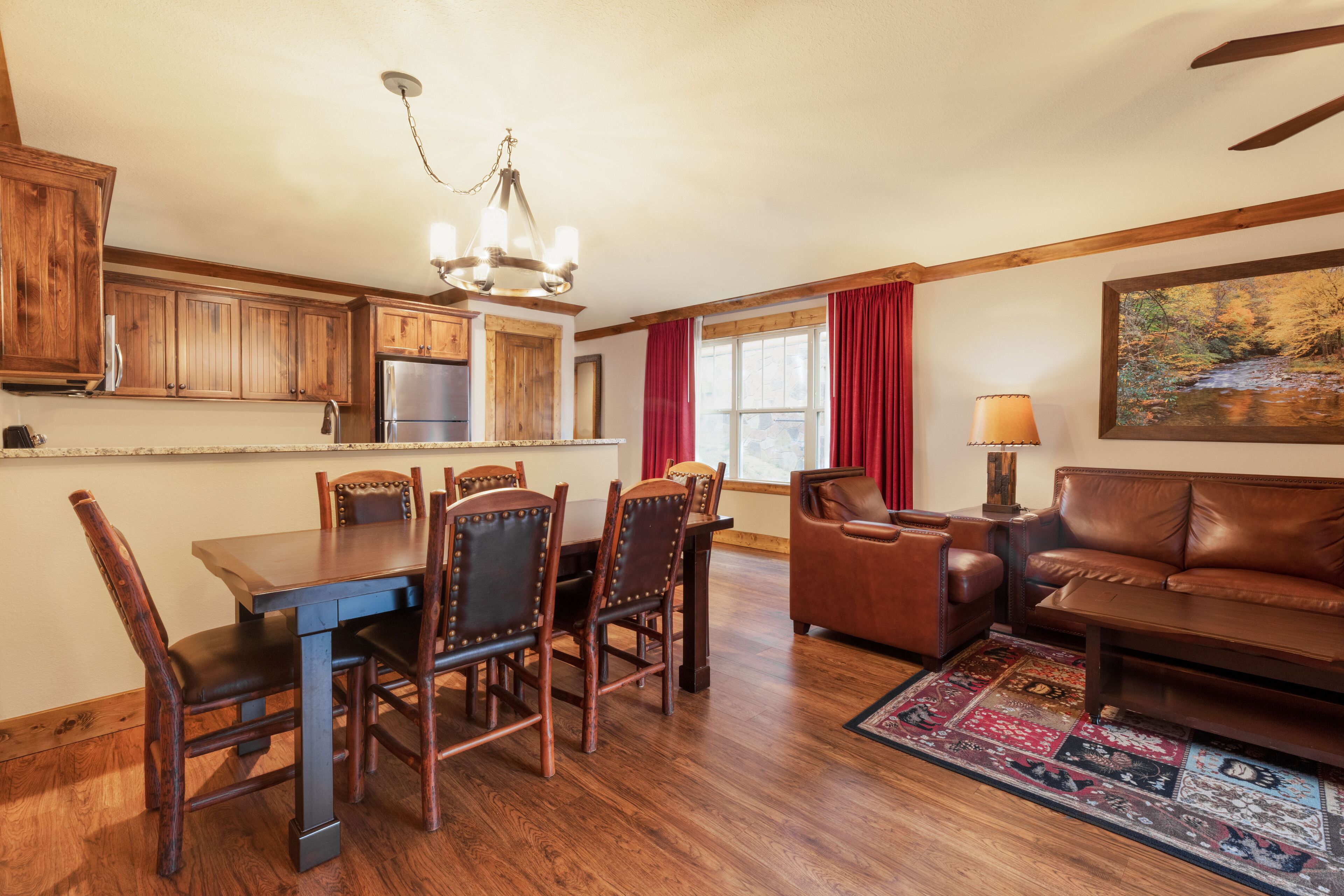 A spacious kitchen with wooden cabinets, a dining table with chairs, a leather sofa, and a rug.