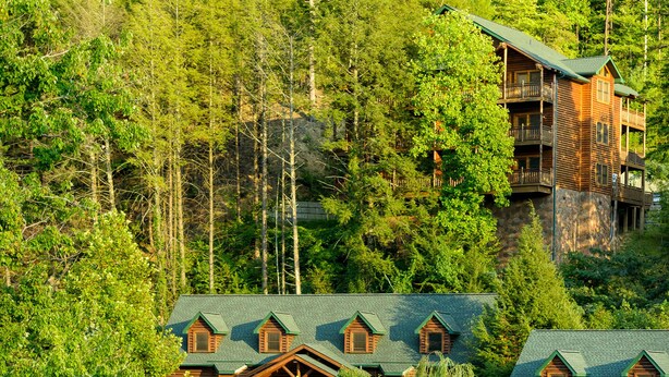 A log cabin-style hotel with multiple balconies, a swimming pool, and lush greenery surrounding the property.