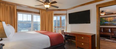 A hotel room with a bed, desk, chair, TV, and a balcony with a view.