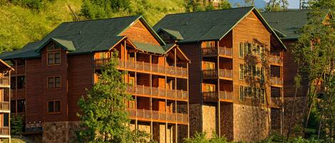 A multi-story lodge with balconies and a stone foundation, surrounded by lush greenery.