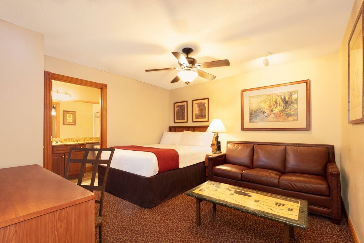 Une chambre d’hôtel comprenant un lit, un canapé en cuir, une table à manger, un ventilateur de plafond et des œuvres d’art accrochées aux murs.