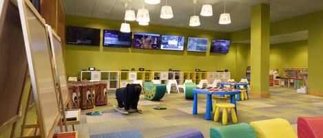 A children's play area with colorful furniture, a whiteboard, and multiple screens on the wall.