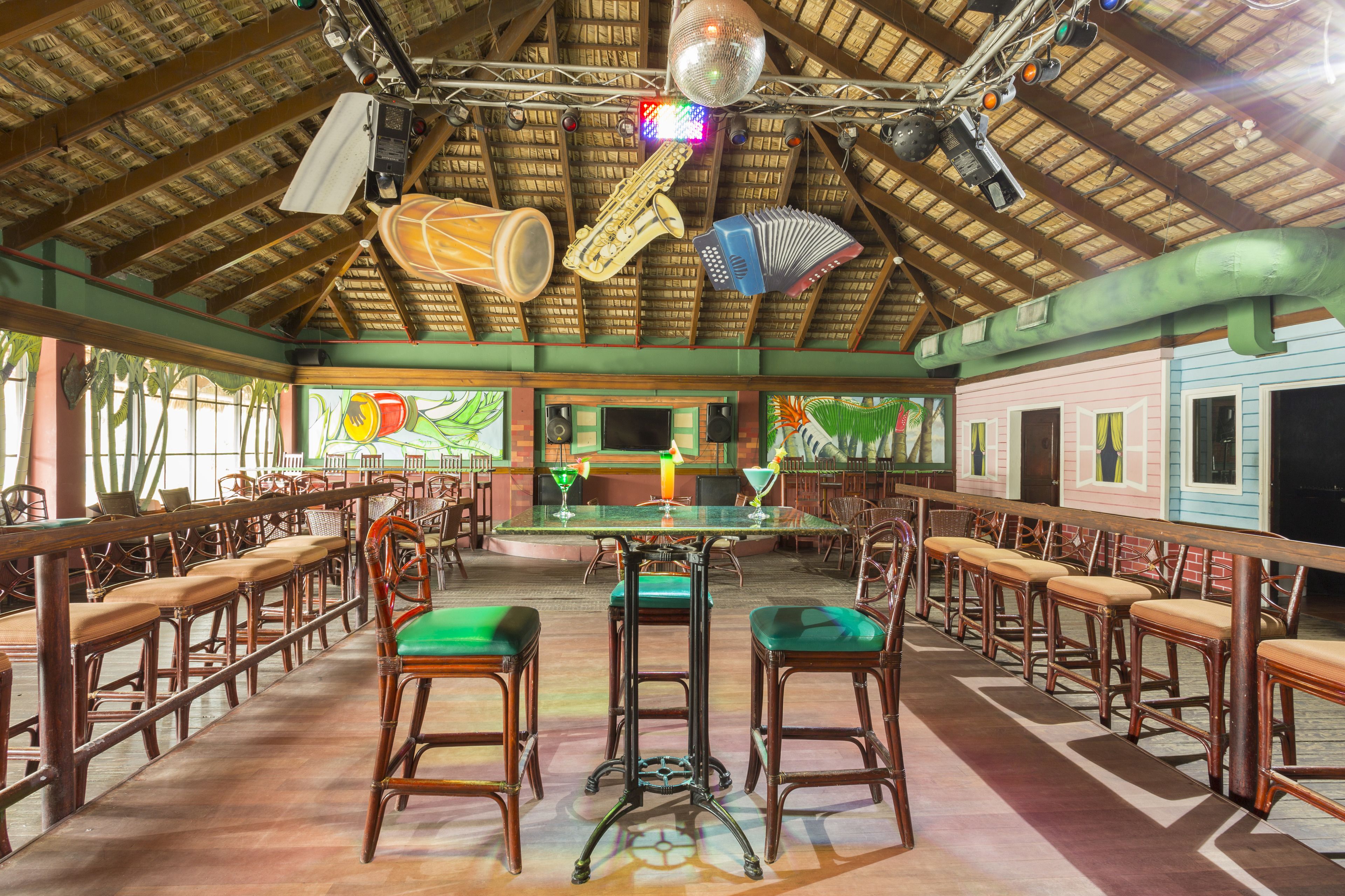 Un restaurant doté de tabourets de bar en bois, d’un plafond haut avec des poutres apparentes et d’une scène où sont disposés des instruments de musique.