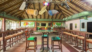 Un restaurant doté de tabourets de bar en bois, d’un plafond haut avec des poutres apparentes et d’une scène où sont disposés des instruments de musique.