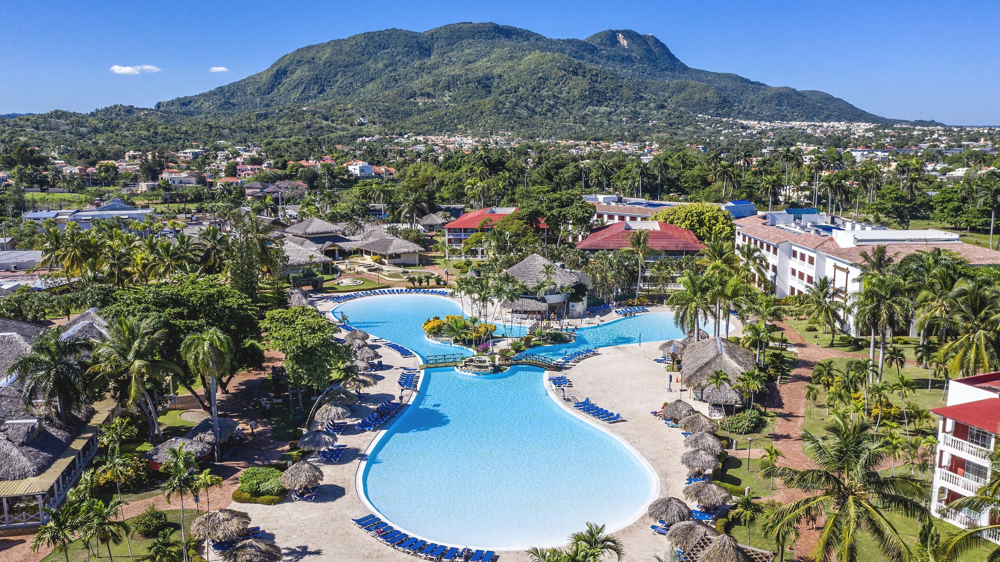 Un resort con una gran piscina, palmeras y una montaña al fondo.