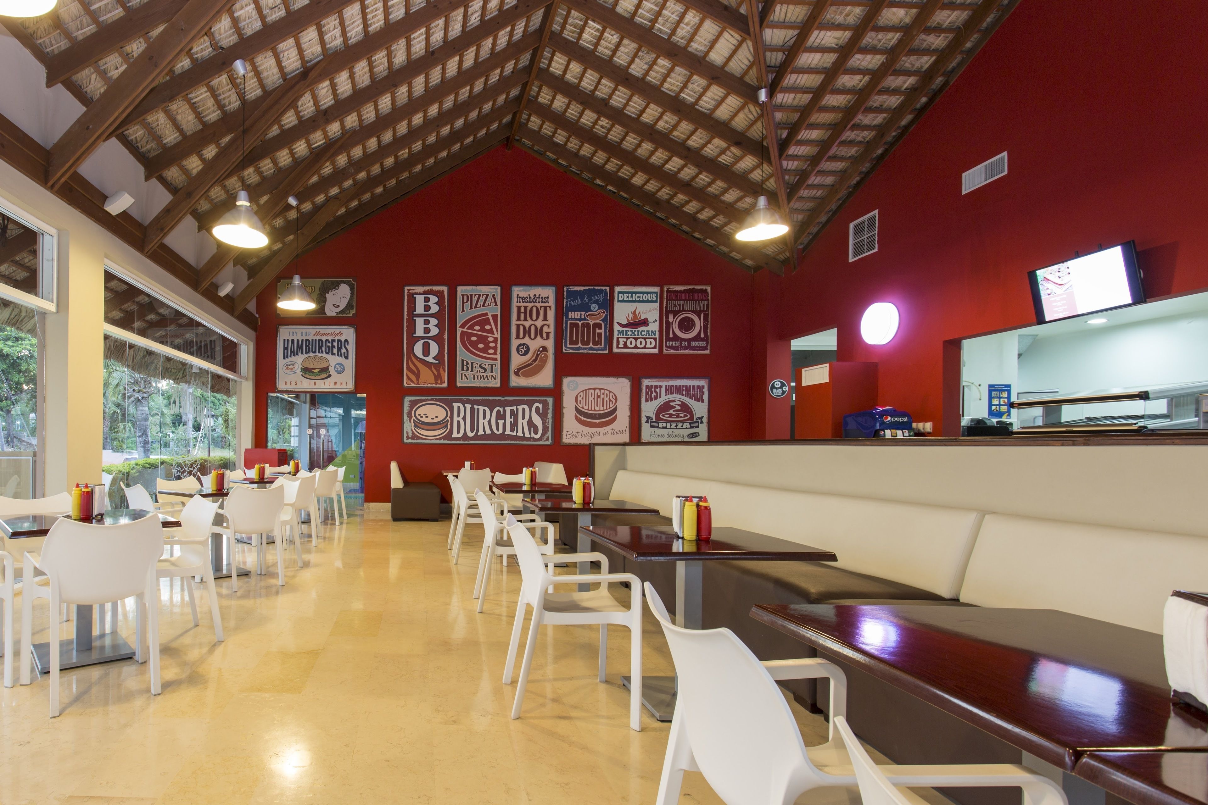 Un restaurant à l’intérieur rouge, avec un plafond en bois et des chaises et des tables blanches.