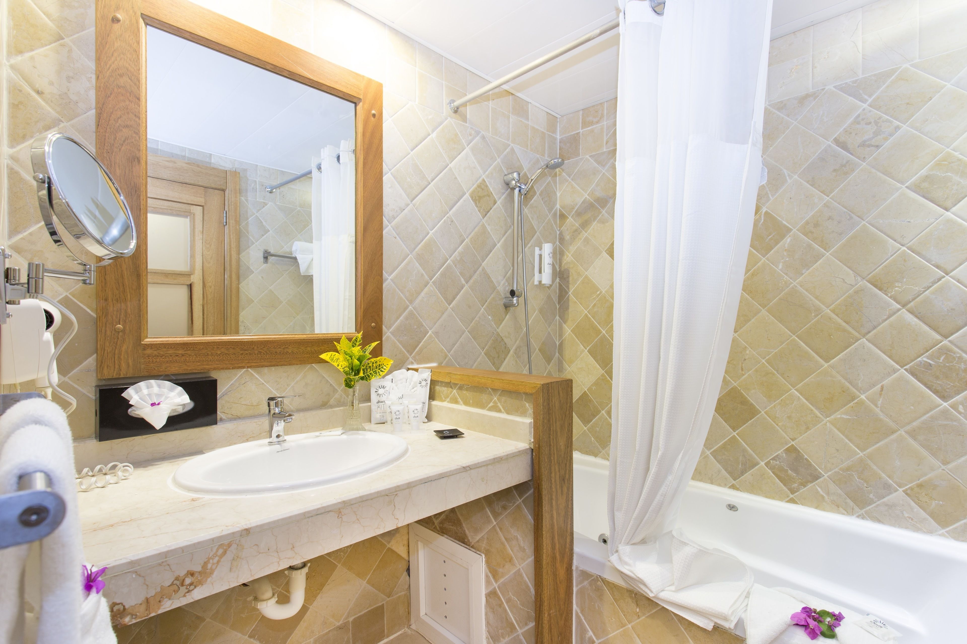 A bathroom with a sink, mirror, shower, and tiled walls.