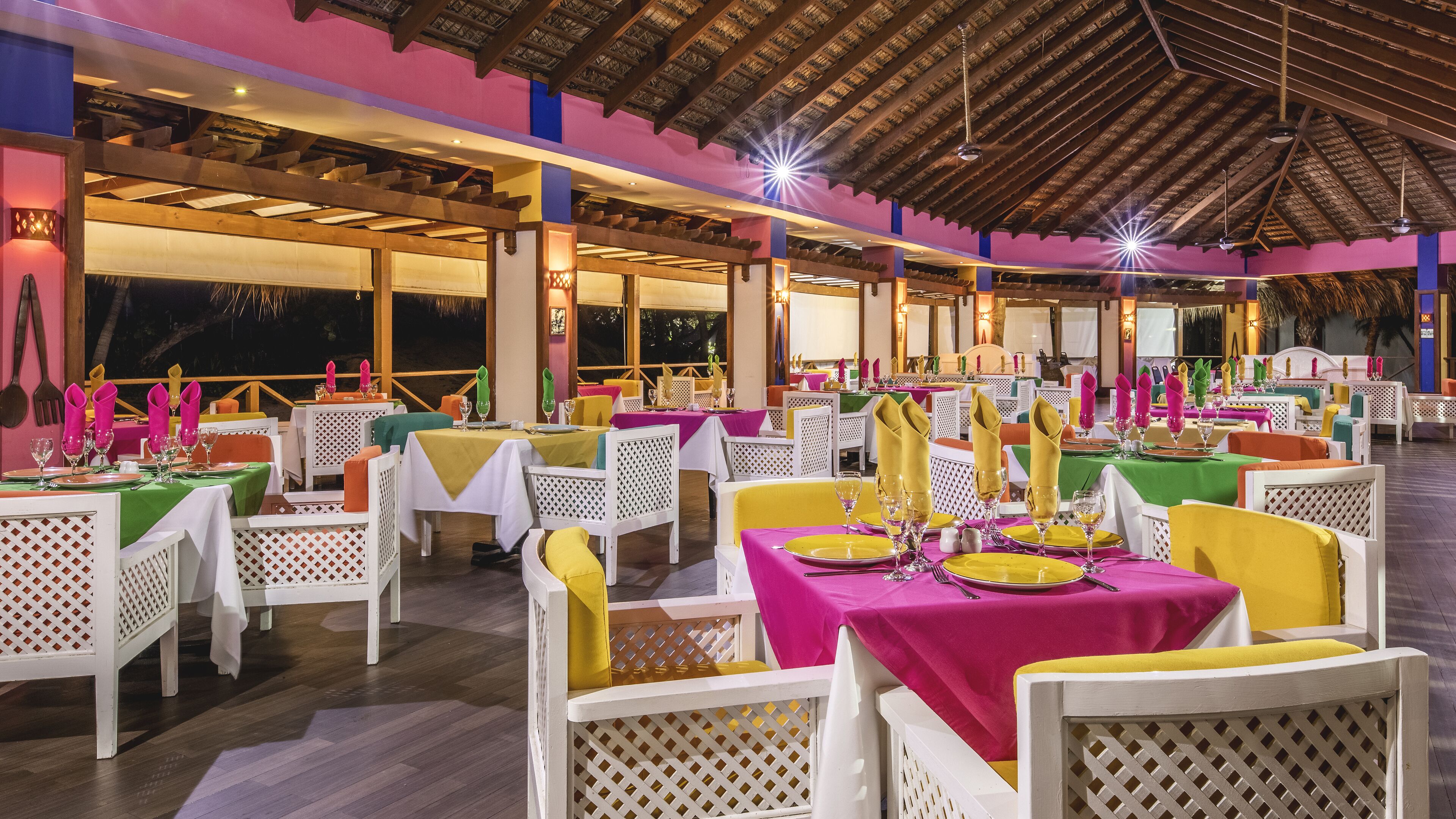 A restaurant with multiple tables set for dining, featuring a variety of tablecloth colors and neatly arranged table settings.