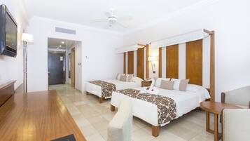 A hotel room with two beds, a wooden desk, a TV, and a ceiling fan.