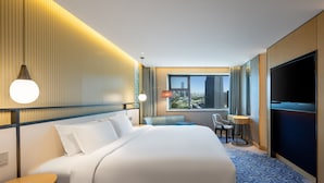 Una habitación de hotel con una cama grande, un escritorio, una silla, un televisor y una ventana con vista a la ciudad.