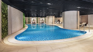 Una piscina interior con suelo de baldosas, sillones de descanso y un techo con diseño lineal.