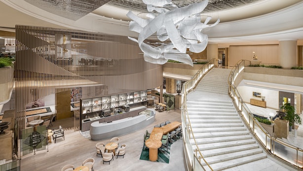 Un amplio vestíbulo de hotel con un bar central, varias zonas de estar y una imponente escalera.