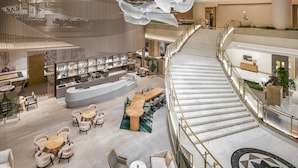 Un amplio vestíbulo de hotel con una recepción central, varias zonas de estar y una imponente escalera.