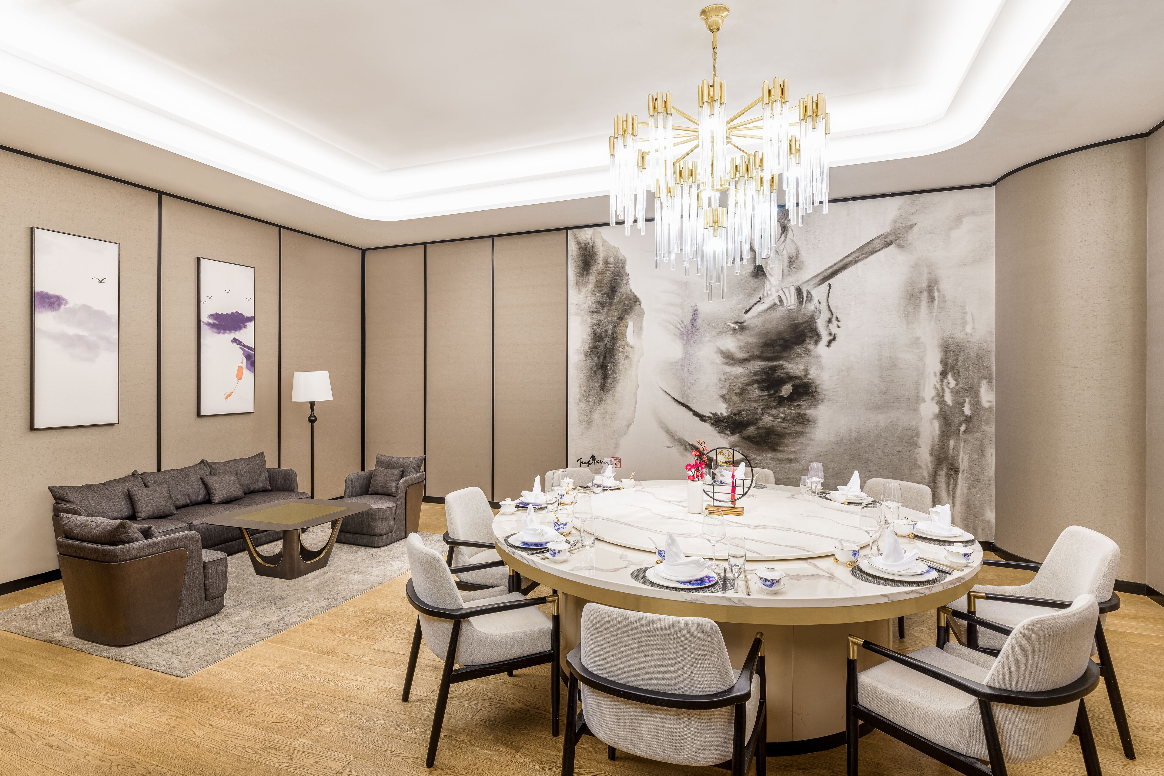 A modern dining area with a round table set for six, surrounded by six chairs. A large abstract painting adorns the wall behind the table.