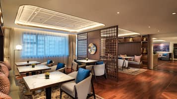 A modern hotel lobby with seating areas, a reception desk, and a large window with curtains.