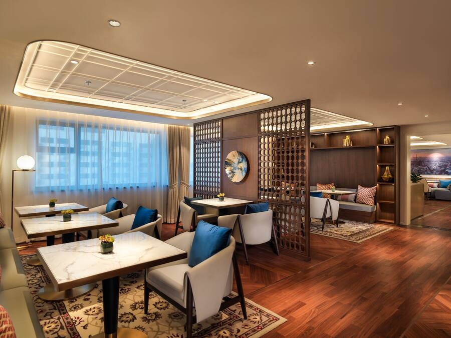 A modern hotel lobby with seating areas, a reception desk, and a large window with curtains.
