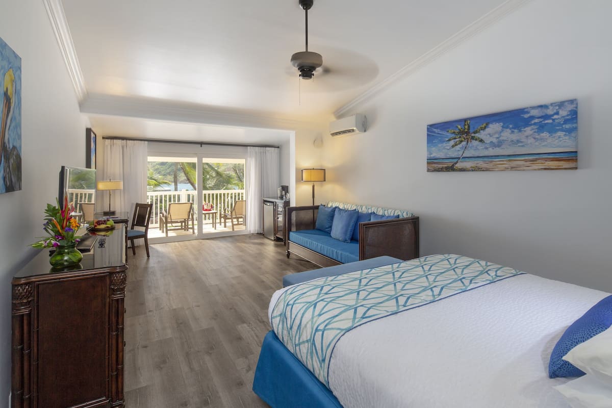 Ein Hotelzimmer mit Bett, Sofa, Essbereich und einem Balkon mit Blick auf den Strand.
