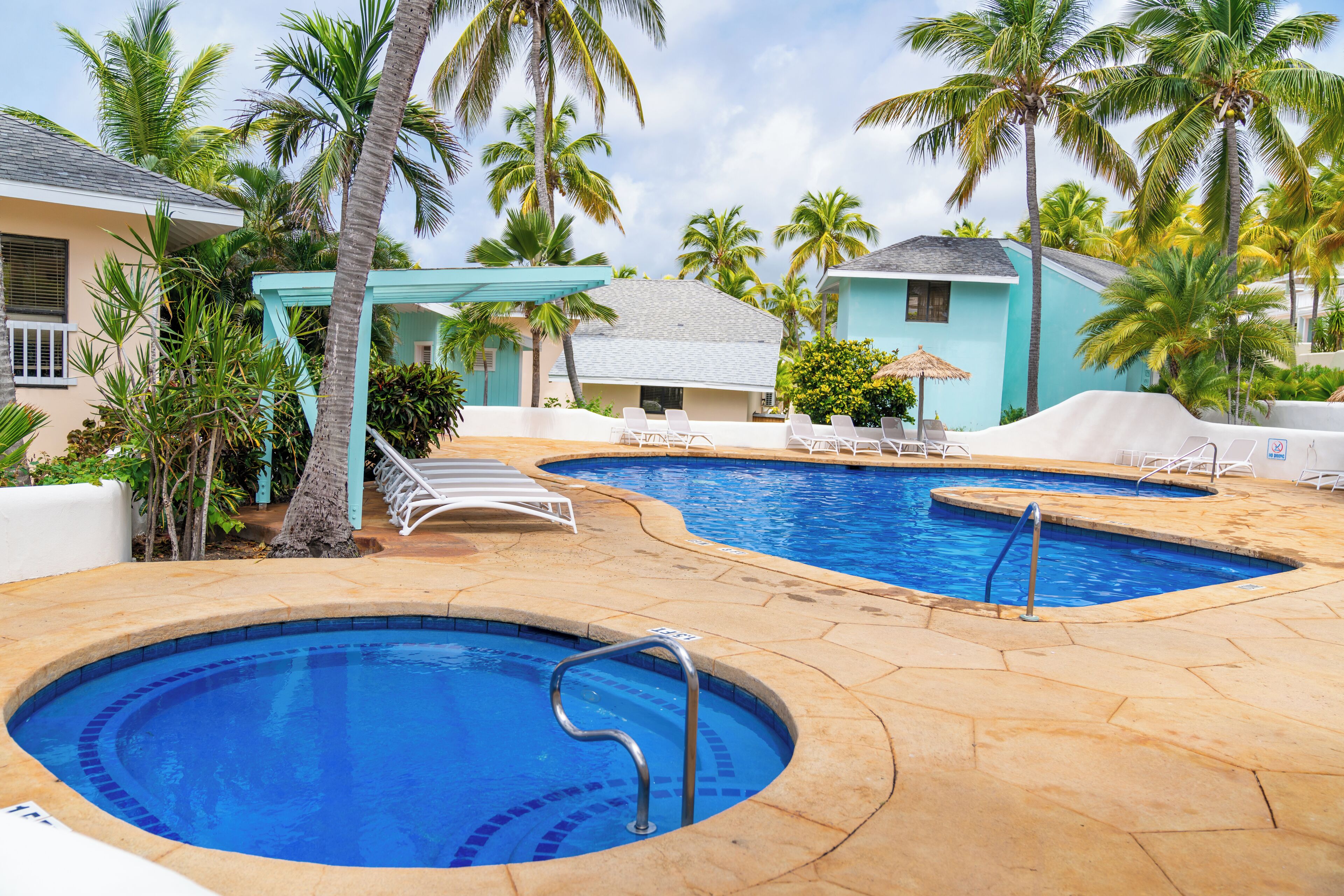 Un área de piscina con dos piscinas, sillas de descanso y palmeras.