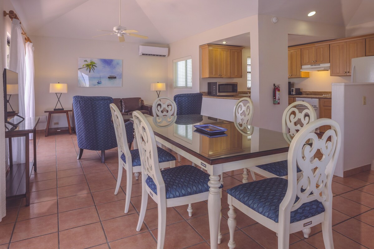 A dining area with a glass table, white chairs, and a blue patterned sofa.