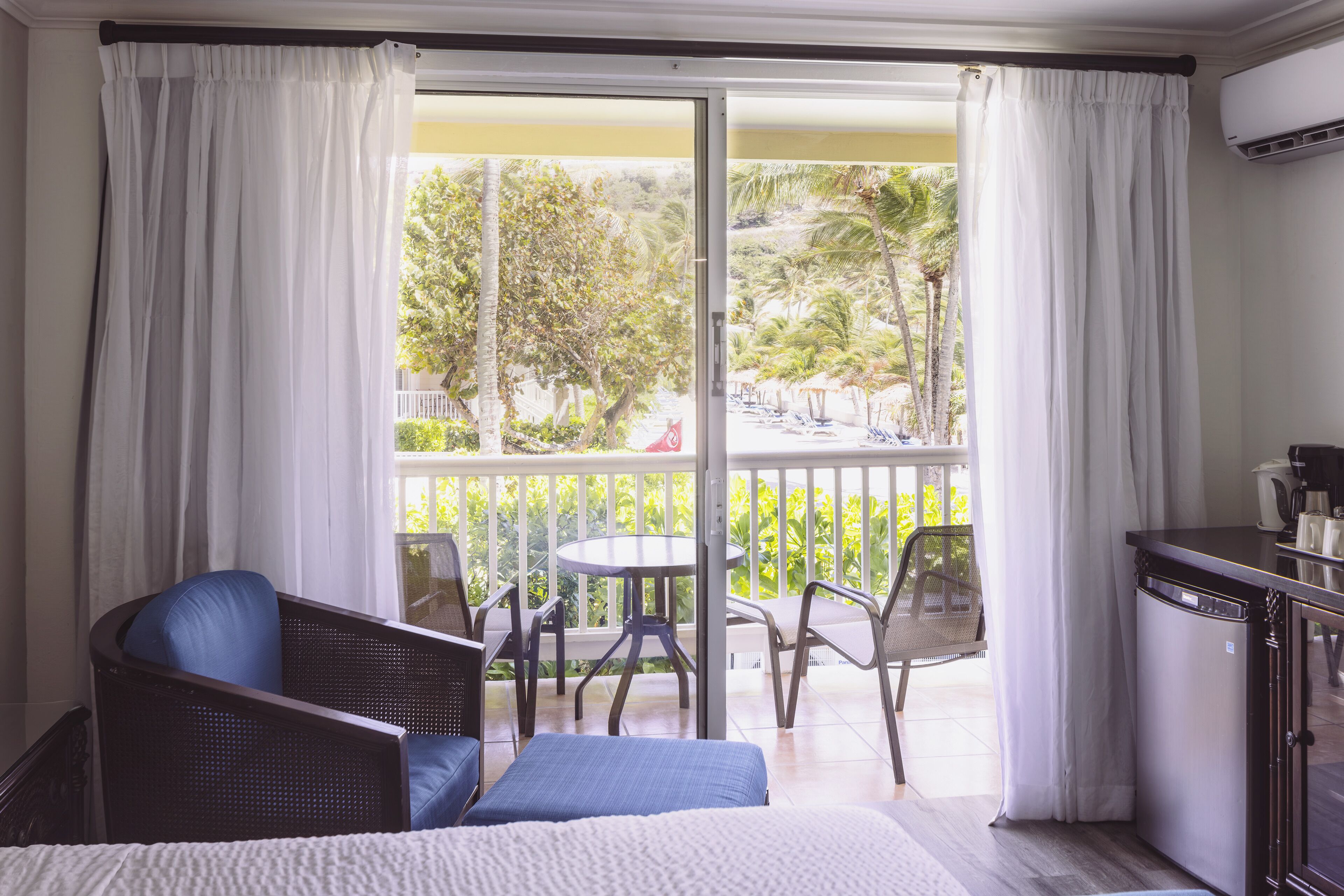 A hotel room with a balcony, a bed with a blue pillow, a small table, and chairs.