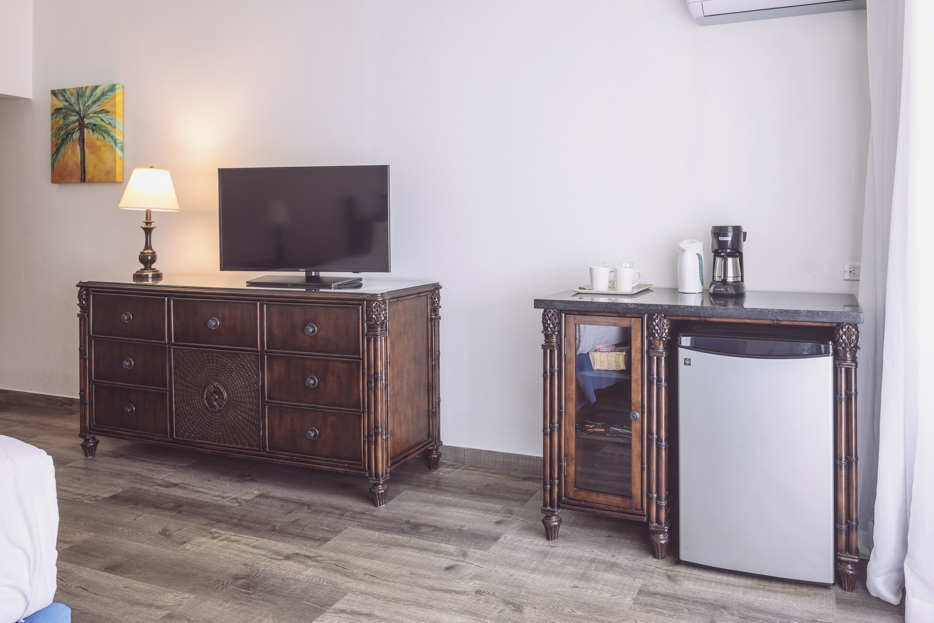 A hotel room with a wooden dresser, a television, a coffee maker, and a refrigerator.