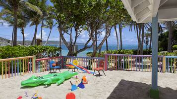 Children can play safely in this enclosed play area with slides, swings, and a fun float, overlooking the ocean and palm trees.