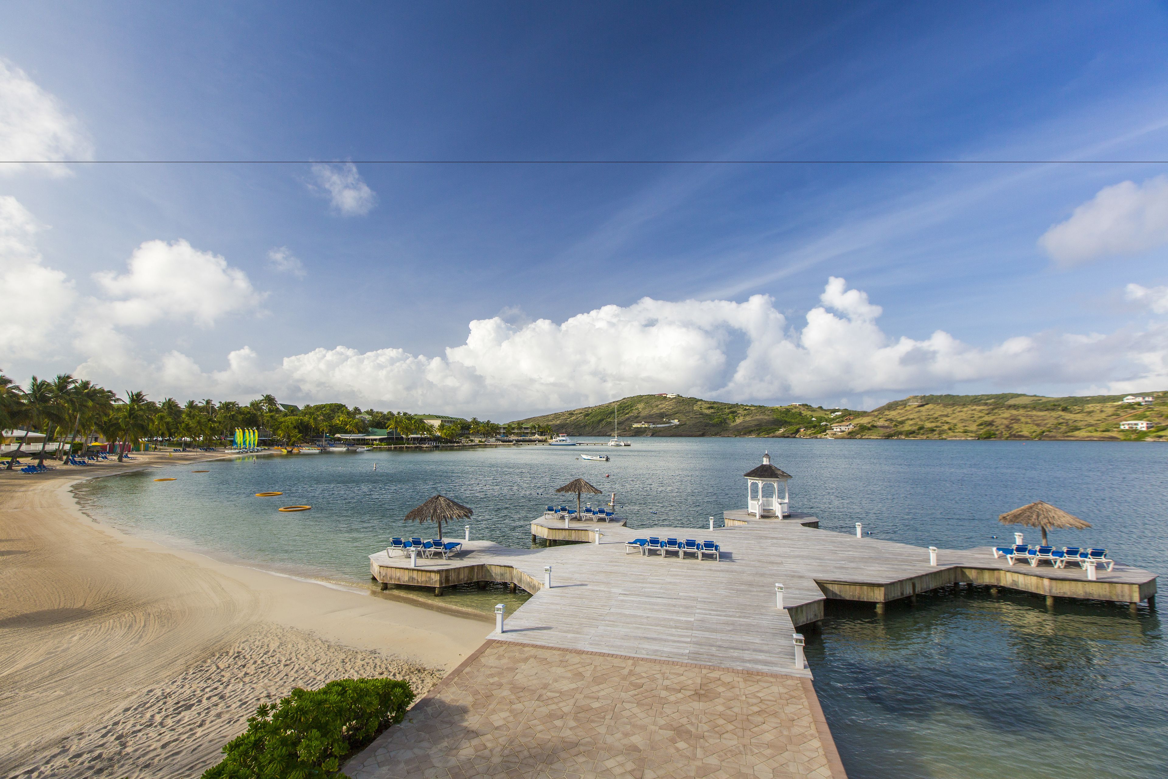 A beachside pier with lounge chairs and a gazebo, overlooking calm waters and a sandy beach.