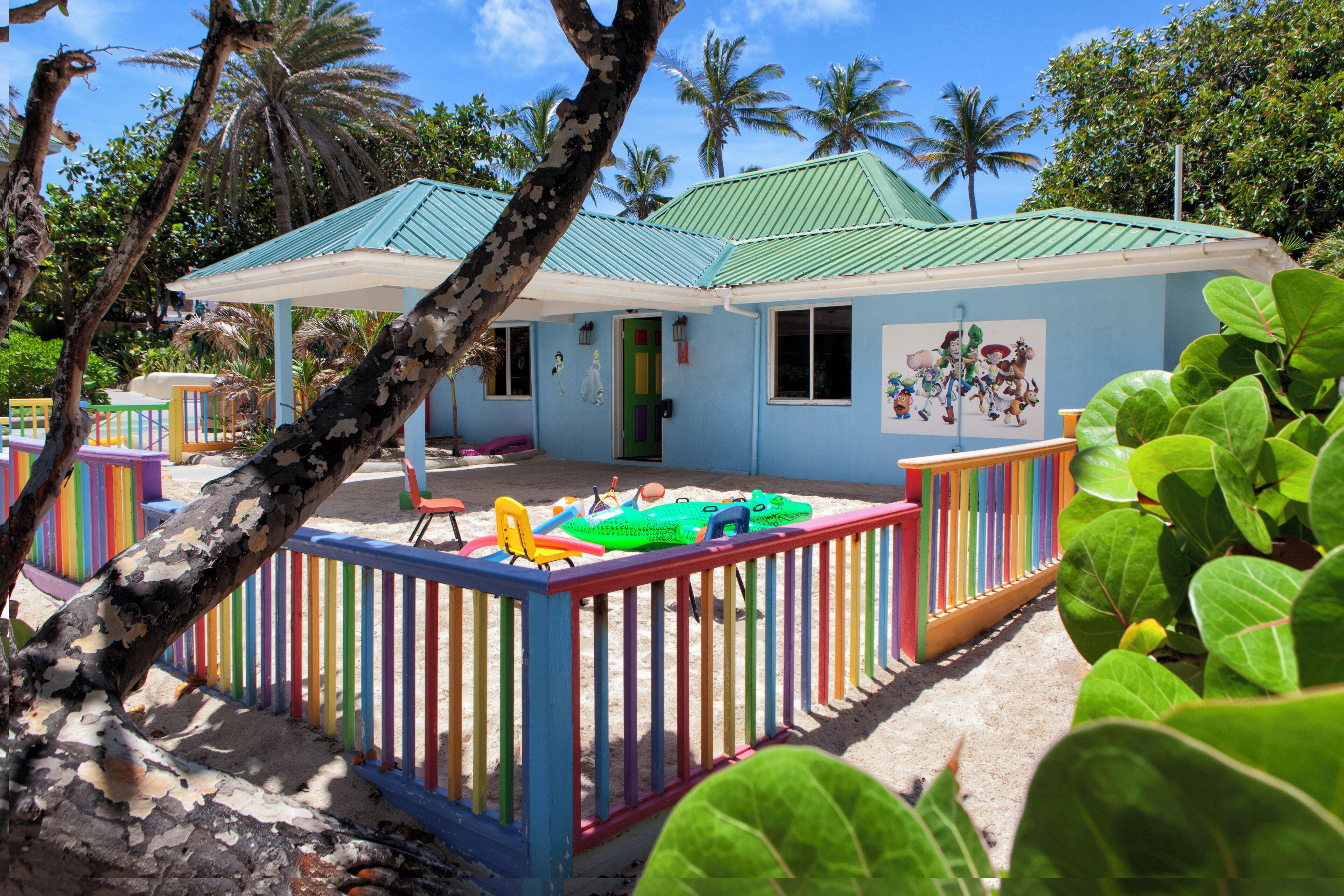 Una casa de playa con un cerco colorido, un porche cubierto y un mural de personajes animados.