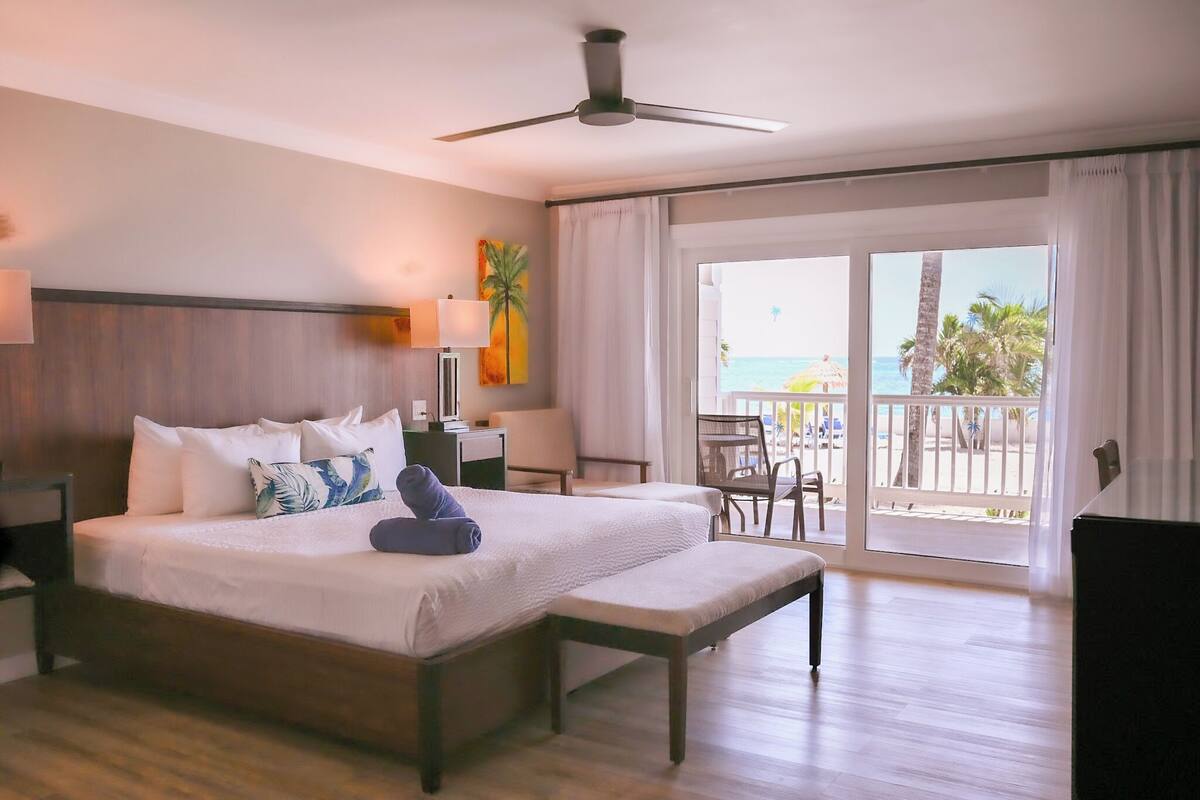 Ein Hotelzimmer mit Bett, Schreibtisch, Stuhl, Balkon mit Meerblick und Deckenventilator.