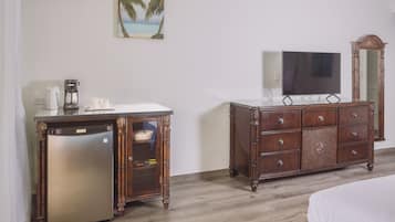 A hotel room with a bed, a wooden dresser, a refrigerator, a coffee maker, a television, and a wall-mounted air conditioner.