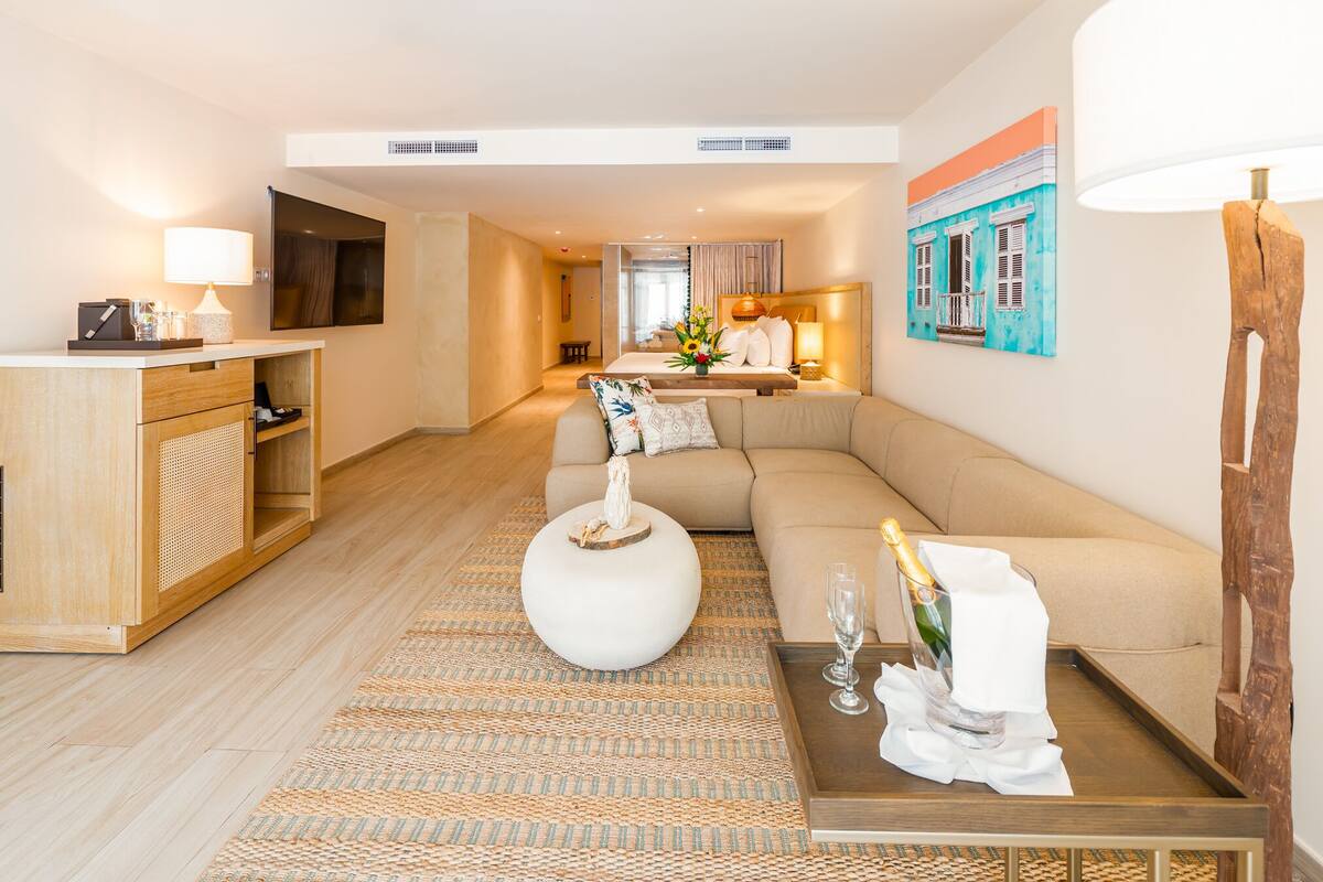 A modern hotel room with a sofa, a round coffee table, a wooden sideboard, and a painting on the wall.