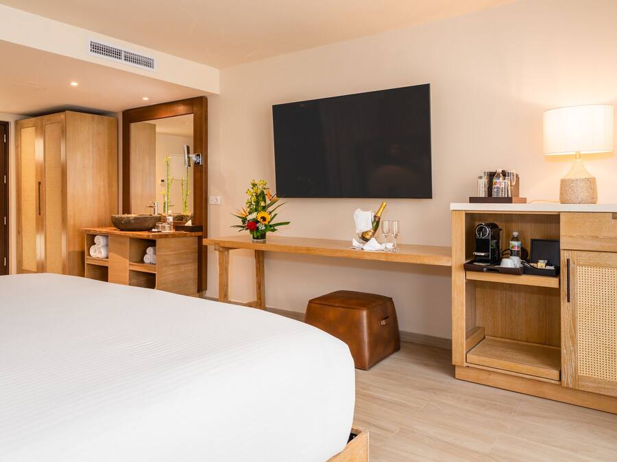 Habitación de hotel con una cama grande, armario de madera, escritorio con lámpara, televisor de pantalla plana y un taburete pequeño.