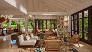 A spacious living area with a high ceiling, large windows, and a variety of seating options including a sofa, chairs, and a coffee table. - Zoetry Curaçao Resort & Spa - All Inclusive (Willemstad)