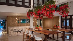 A reception area with a wooden reception desk, bar stools, and hanging red flowers. - Zoetry Curaçao Resort & Spa - All Inclusive (Willemstad)