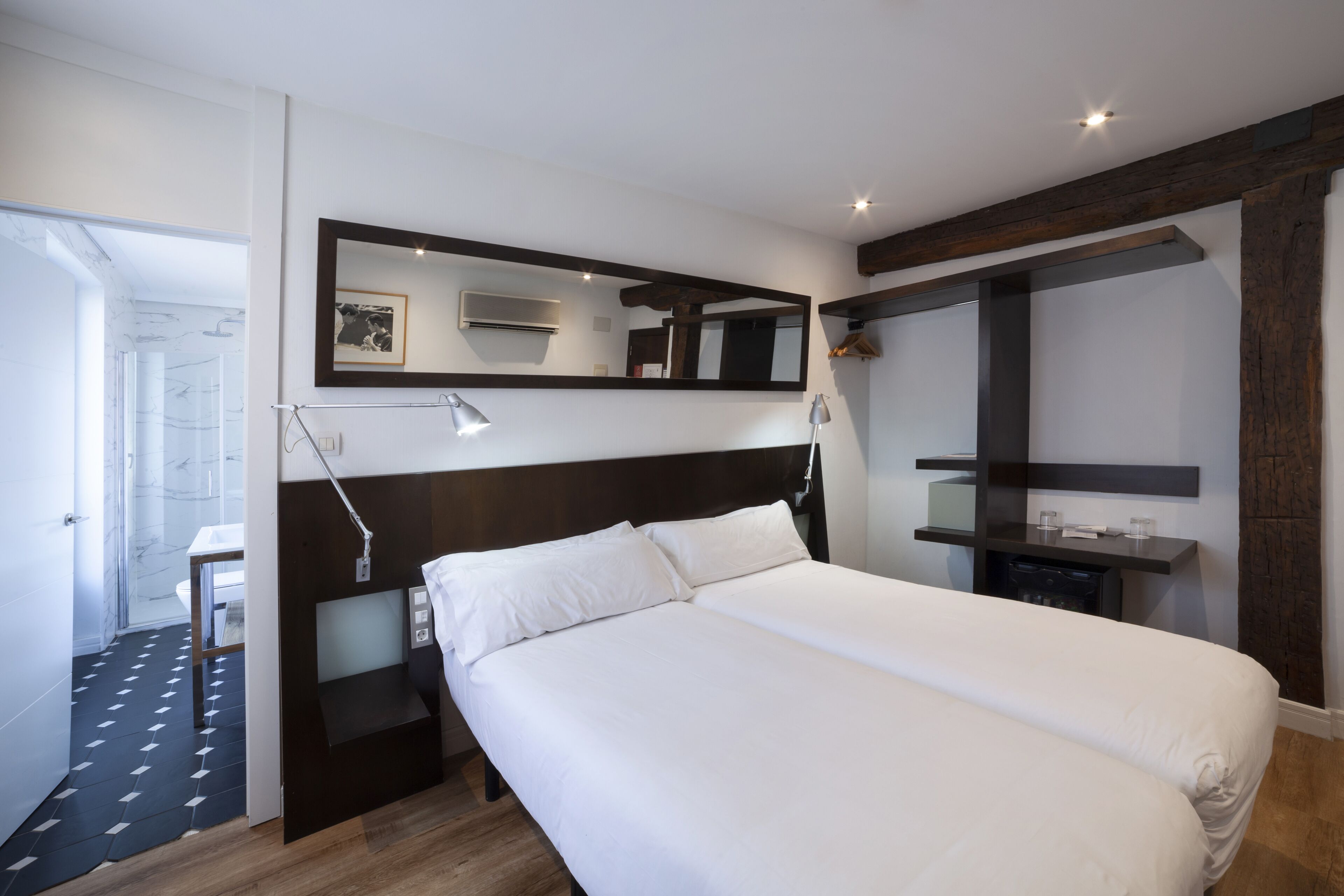 Una habitación de hotel moderna con una cama grande, una mesita de noche, un espejo y un pequeño escritorio con una silla.