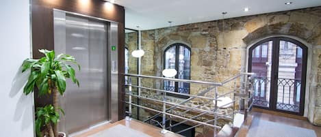 Un hall d’entrée moderne avec un mur en pierre, un ascenseur, un escalier et une plante en pot.