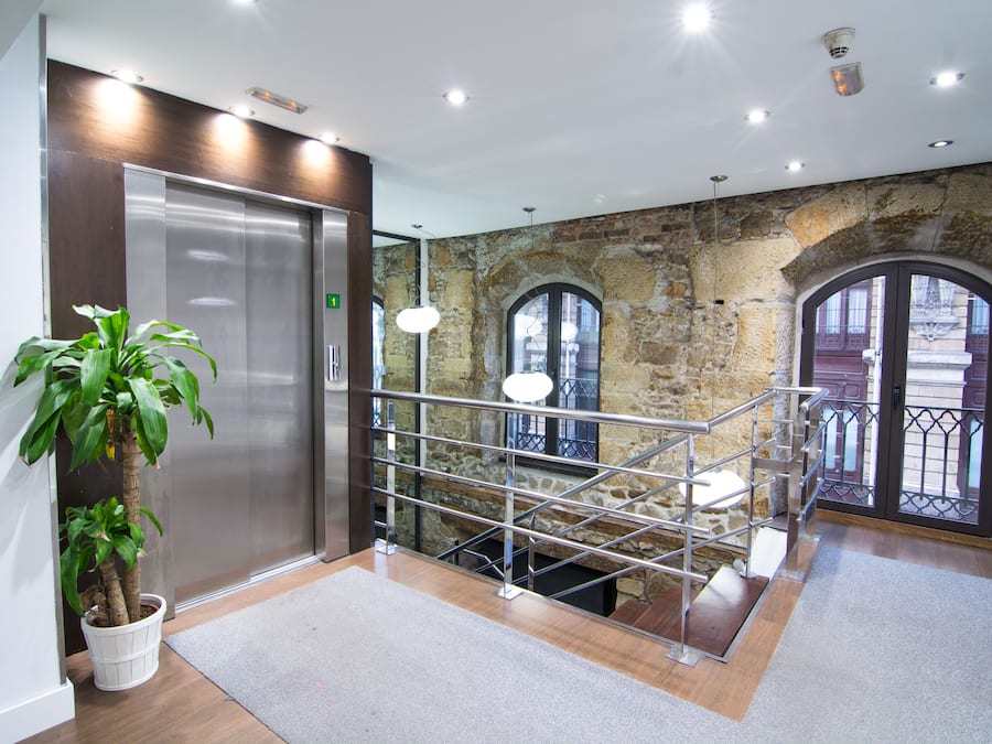 Un vestíbulo moderno con pared de piedra, un ascensor, una escalera y una planta en maceta.
