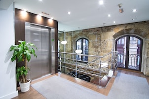 Um hall moderno com parede de pedra, um elevador, uma escadaria e um vaso de planta.