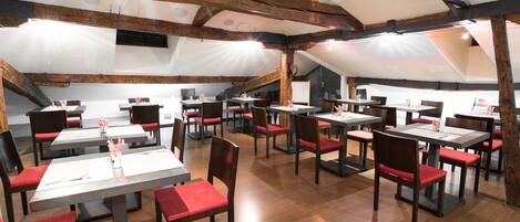 A restaurant with wooden beams, red cushioned chairs, and white tables.