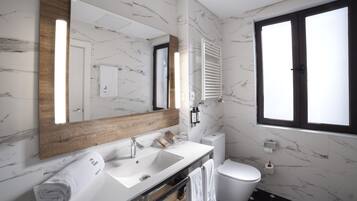Een moderne badkamer met een marmeren spatwand, een houten wastafelmeubel, een grote spiegel, een toilet en een raam voor natuurlijk licht.