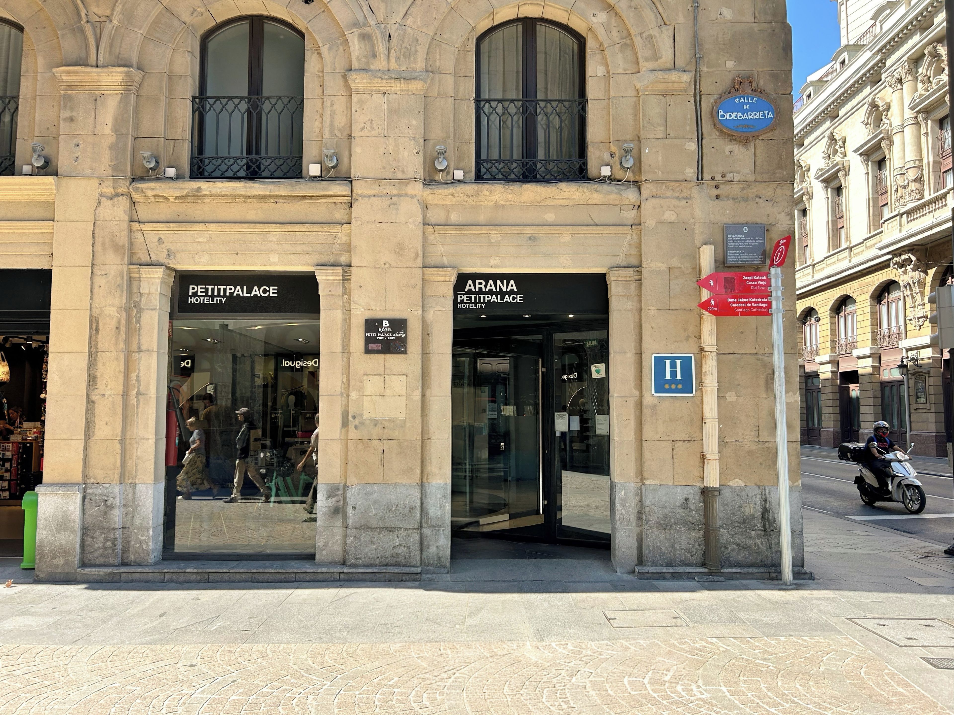 A historic building with two hotel entrances, a pedestrian sign, and a street with a scooter.