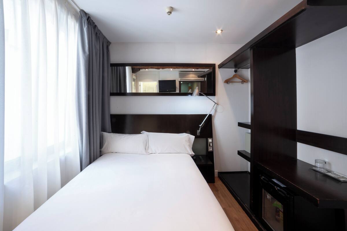 A hotel room with a large bed, a bedside table, a mirror, a wardrobe, and a TV.